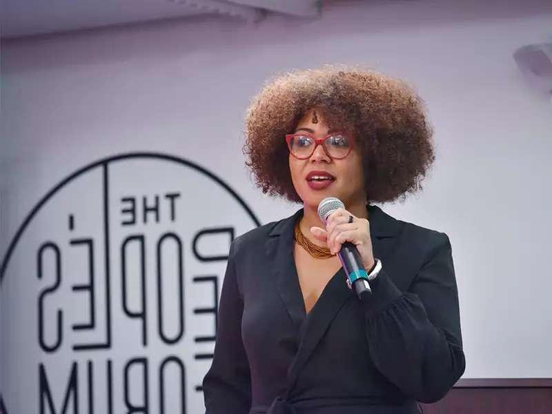 A young Black woman holding a microphone, speaking at an event